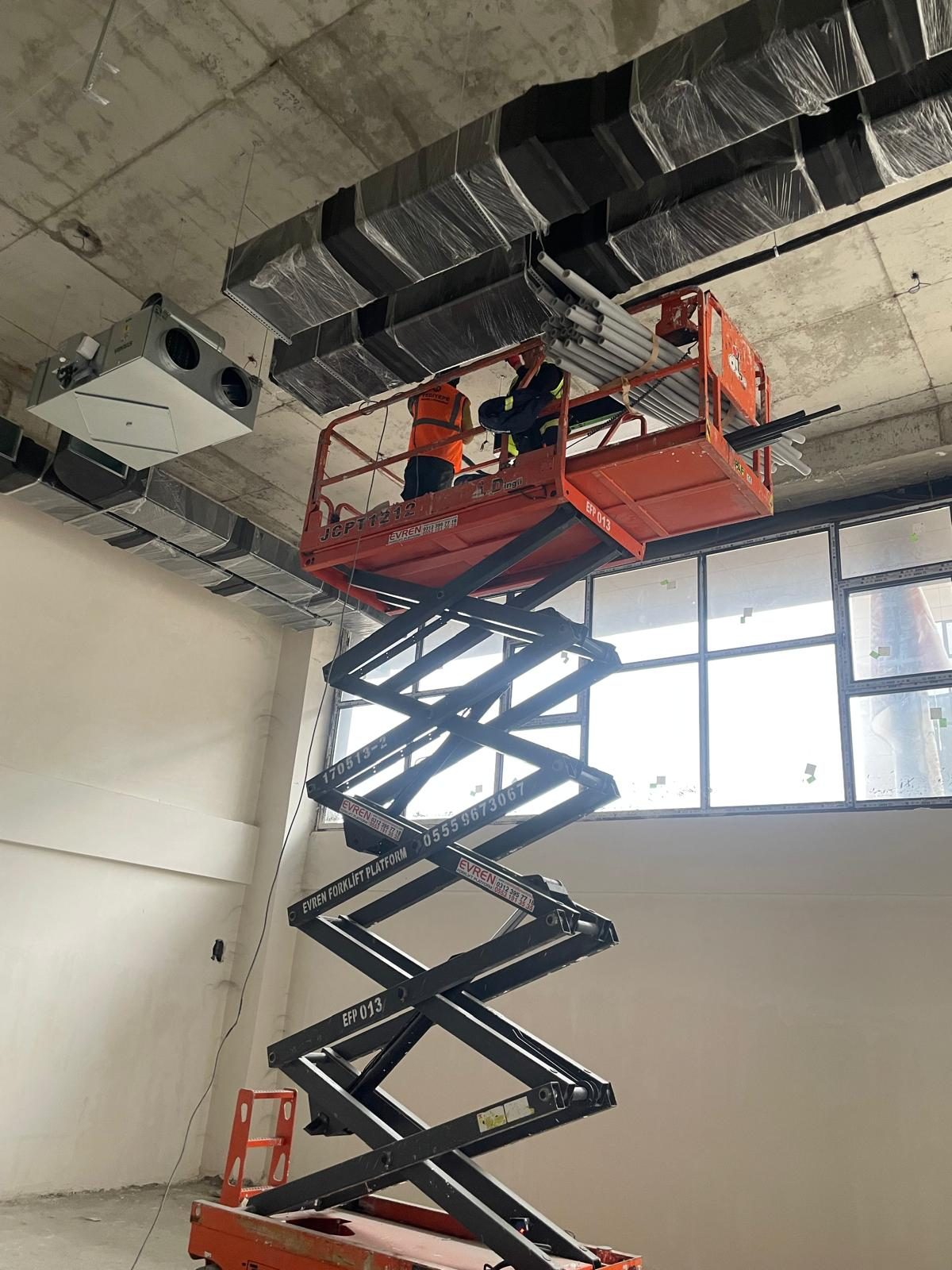 Crew on a scissor lift coordinating HVAC ducts and the plenum against the slab